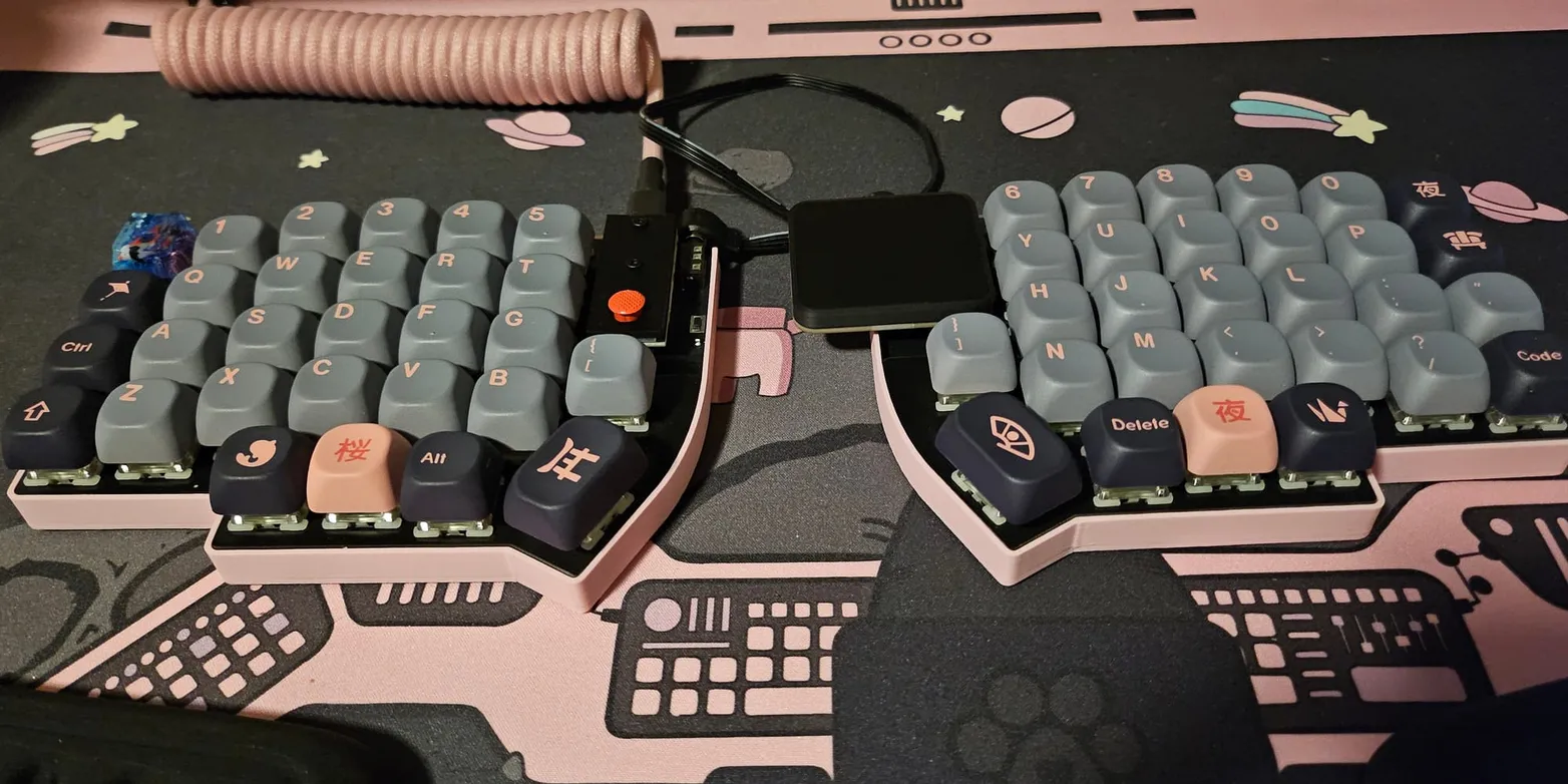 A Lily58 split keyboard in a pink case with grey and navy keycaps, a red trackpoint on the left half and a square touchpad module between the halves